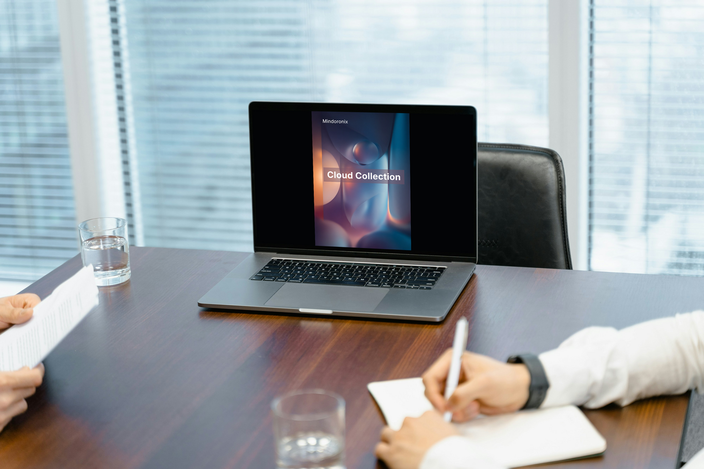 Laptop on a desk with people taking notes in an office setting
